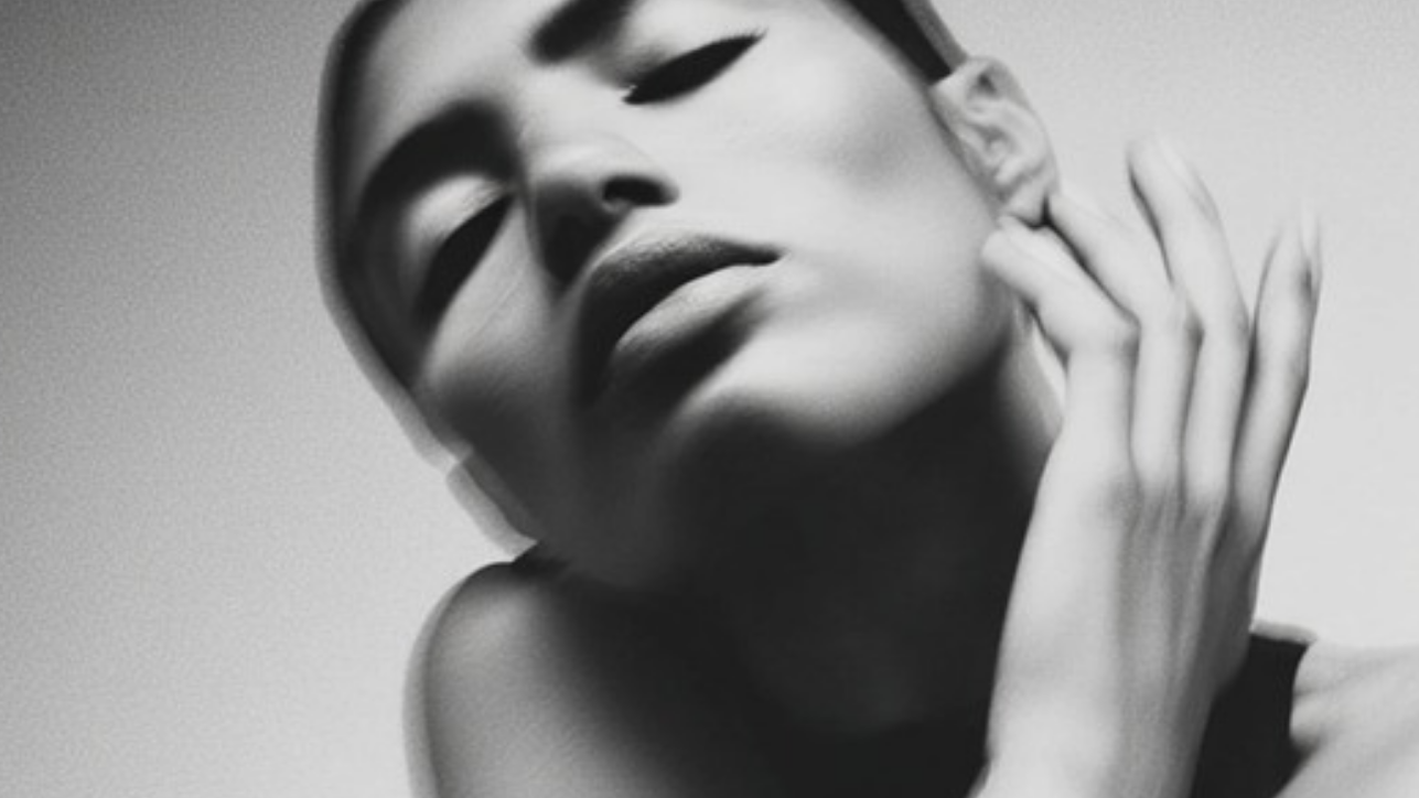 Black and white portrait of a person with one hand on their face against a plain background